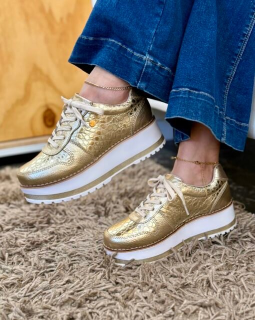 Zapatillas Riviera Dorado: Brillo y Confort Las zapatillas Riviera Dorado fusionan el estilo urbano con un acabado metálico dorado que no pasa desapercibido. Su capellada de cuero premium ofrece un brillo duradero, ideal para quienes buscan un calzado que combine sofisticación y versatilidad. Cuero Premium con Acabado Metálico El cuero dorado se trata con un recubrimiento especial que resiste arañazos y mantiene su tonalidad con el paso del tiempo. Cada pieza se moldea a mano para garantizar una silueta impecable. Comodidad Transpirable Su plantilla de cuero suave y transpirable amortigua el impacto en cada pisada, manteniendo tus pies secos y cómodos durante todo el día. La mediasuela aporta ligereza sin comprometer la estabilidad. Ajuste Ergonómico Con horma normal, las Riviera Dorado se adaptan perfectamente a la forma del pie. Recomendamos tu talla habitual para un ajuste óptimo; su diseño previene rozaduras y puntos de presión. Altura y Estilo La plataforma de 5 cm estiliza tu figura elevando tu postura sin sacrificar confort. La suela de goma antideslizante proporciona tracción en todo tipo de superficies, desde la calle hasta el interior de la oficina. Formas de Combinar Look casual-chic: shorts de lino y camiseta blanca. Oficina moderna: pantalón cropped y blazer oversize. Salidas nocturnas: mini vestido negro y accesorios dorados. Cuidado y Conservación Para mantener el brillo dorado, limpia la capellada con un paño seco y, ocasionalmente, usa un protector de cuero específico. Evita el agua y la exposición prolongada al sol directo. Preguntas Frecuentes ¿Pierde brillo con el uso? Con el cuidado adecuado, el acabado metálico se mantiene intacto. ¿Son aptas para climas cálidos? Sí, la plantilla transpirable evita la humedad y el sobrecalentamiento. Explora Más Modelos Visita nuestra colección completa para descubrir más colores y estilos que se ajusten a tu personalidad.